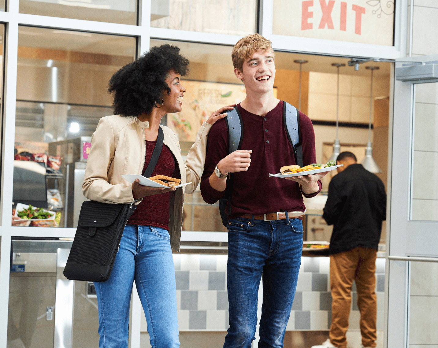 Two students walking at a school with their lunches. 
